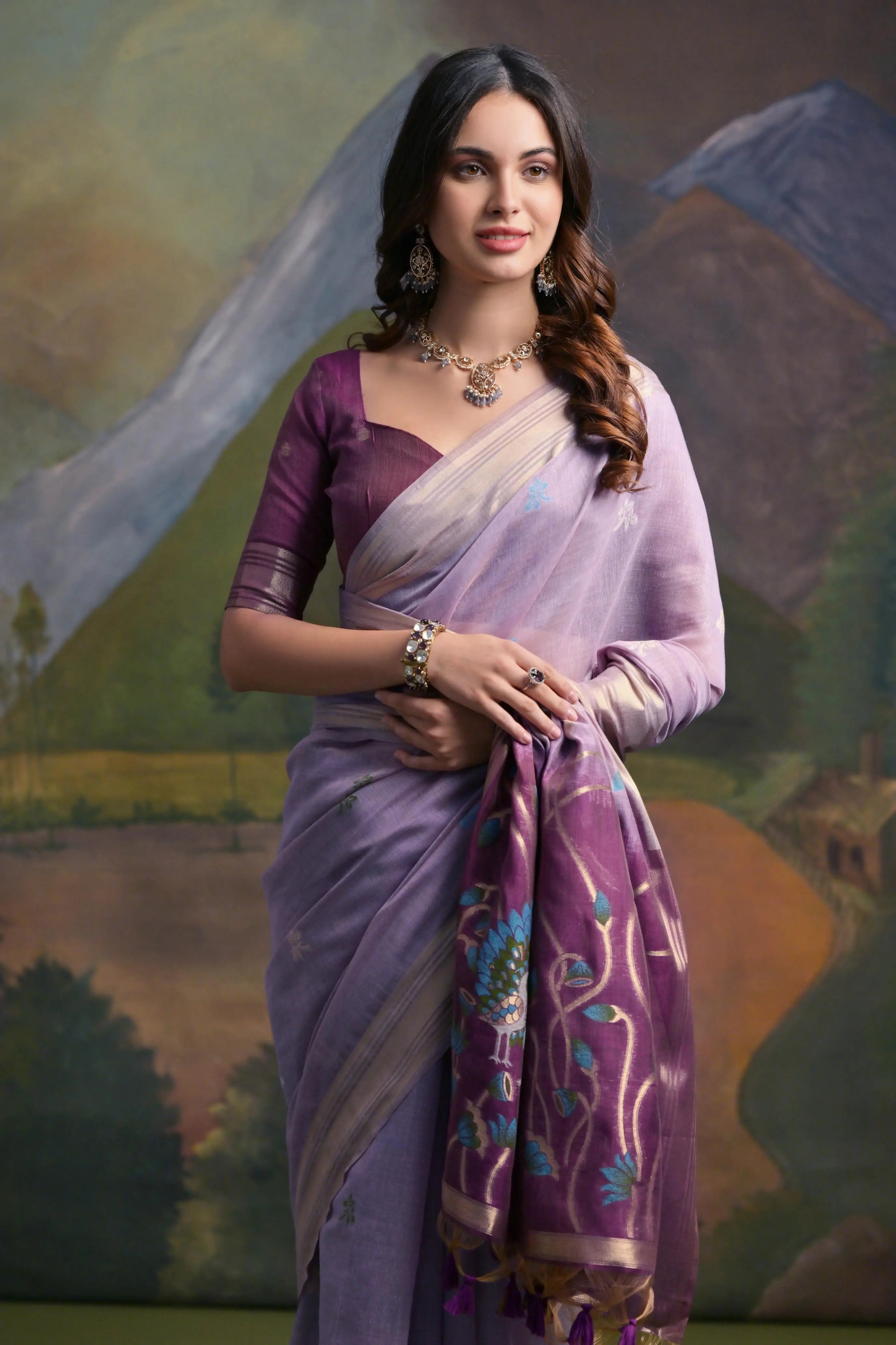 A woman models a soft Lavender Muga Silk Saree with subtle Resham weaving. The pallu dramatically transitions to a deep purple color, featuring intricate blue and purple peacock Resham threadwork. She wears a dark purple blouse and a gold Kundan necklace.